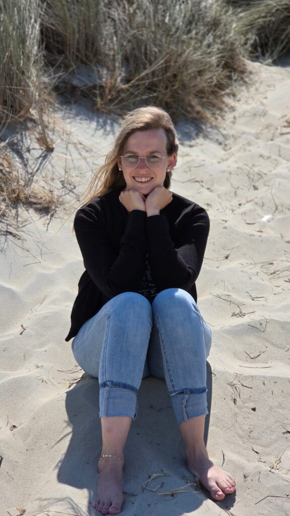 freie Traurednerin Vanessa Grasser sitzt im Sand an der holländischen Küste von Zeeland und hat die Fäuste wie ein Herz. Ihr Kopf ist darauf abgestürzt.